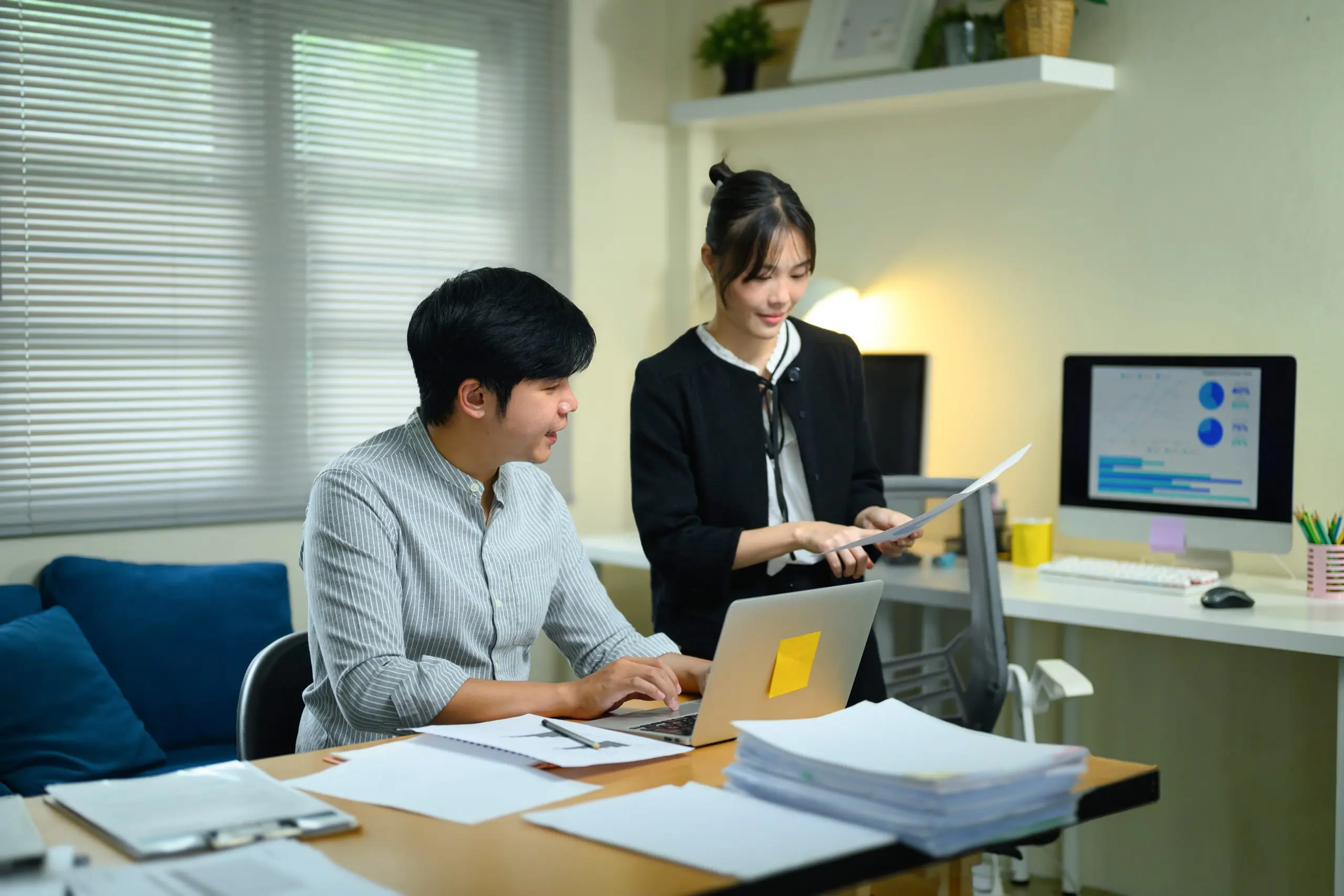 Two business professionals review audit documents and a laptop with charts in a home office
