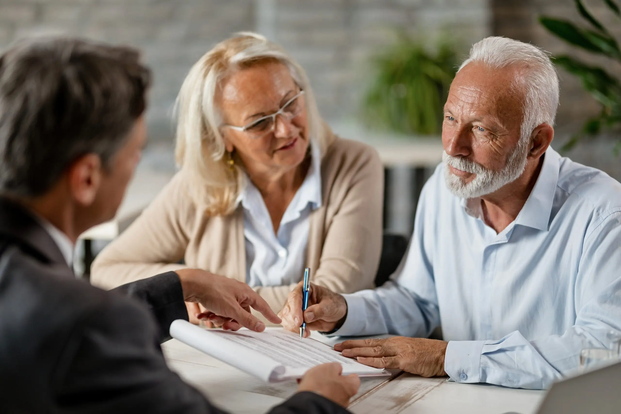 A senior couple signs a document while meeting with an adviser at a table