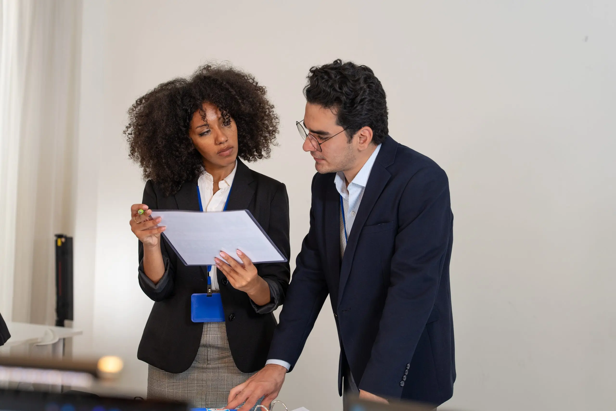 Two colleagues in business attire review a document together in a bright office