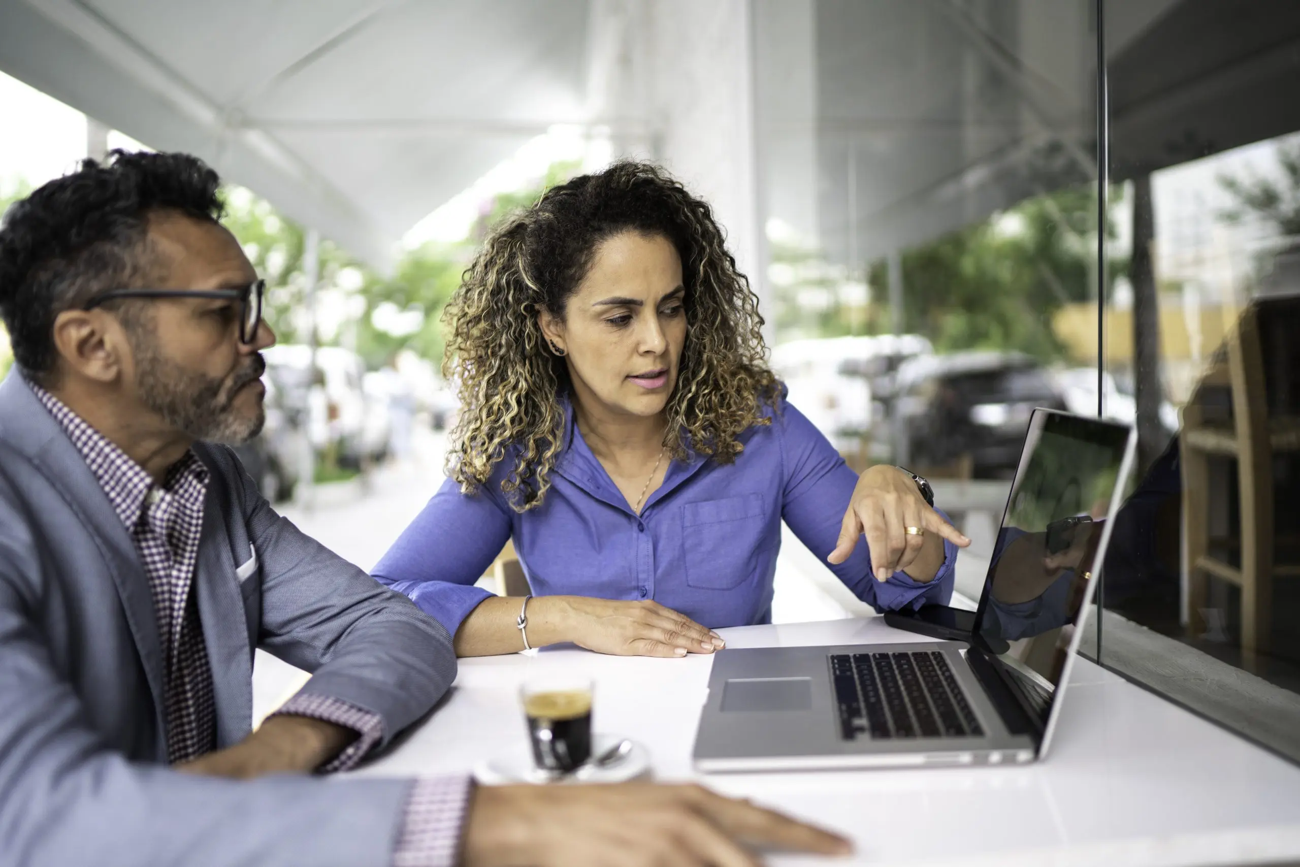 A man and woman review financial documents beside a laptop at a bright cafe table