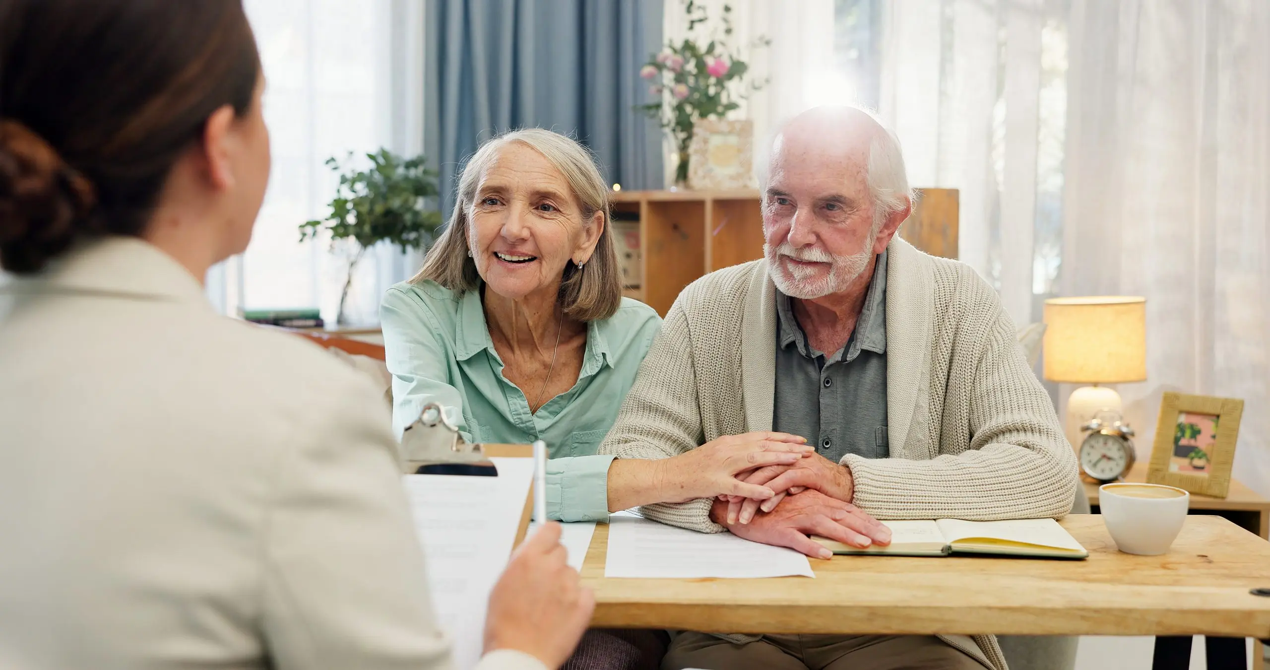 An adviser reviews documents with a smiling older couple at a table in a bright living room